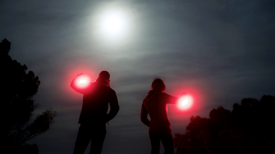 A photo of a silhouette of a couple under the moon at nighttime holding two red lanterns