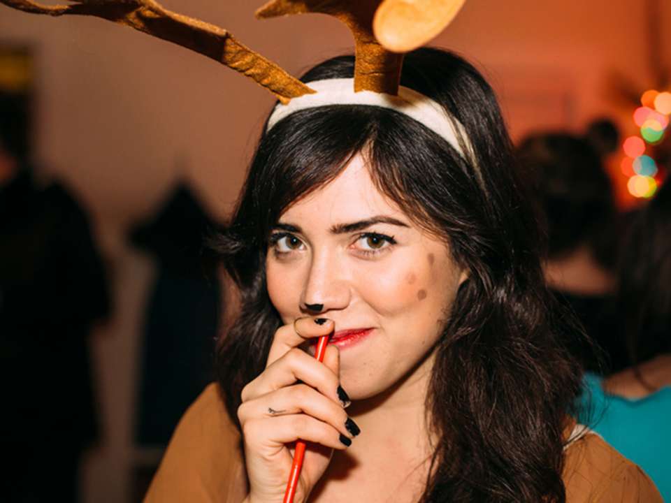 a young woman sips from a drink while dressed in a reindeer costume at a holiday party