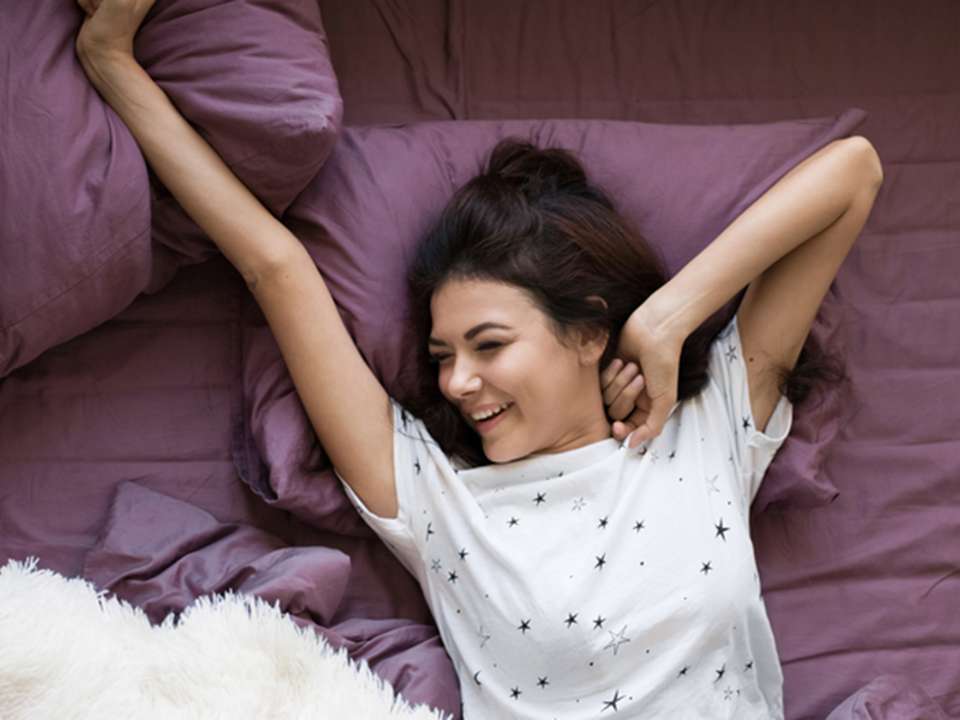 a young smiling woman stretching in bed