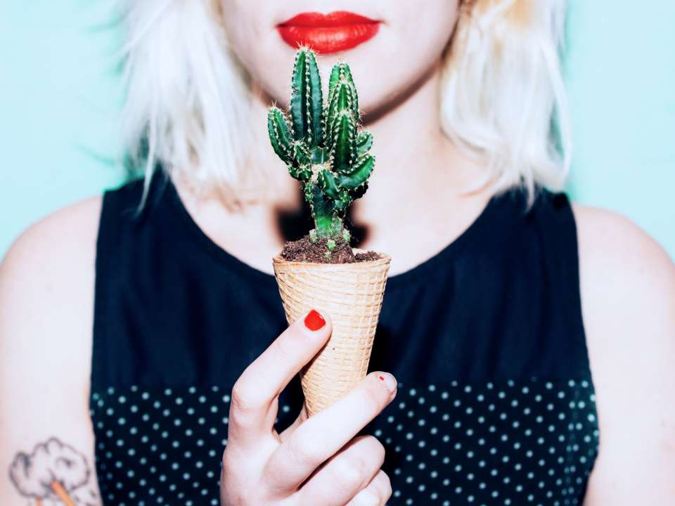 A woman holds a cactus in an ice cream cone.