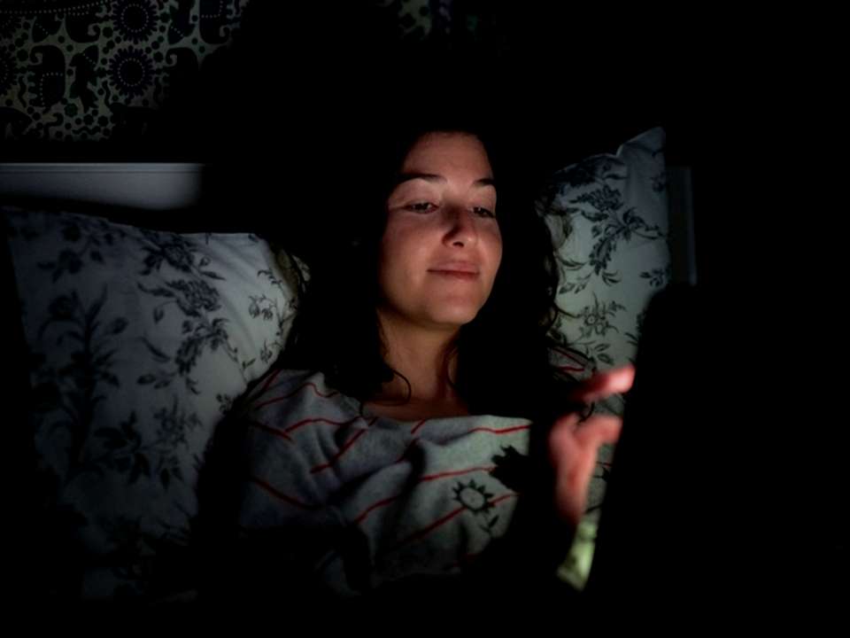 A woman uses a tablet in bed in the dark.