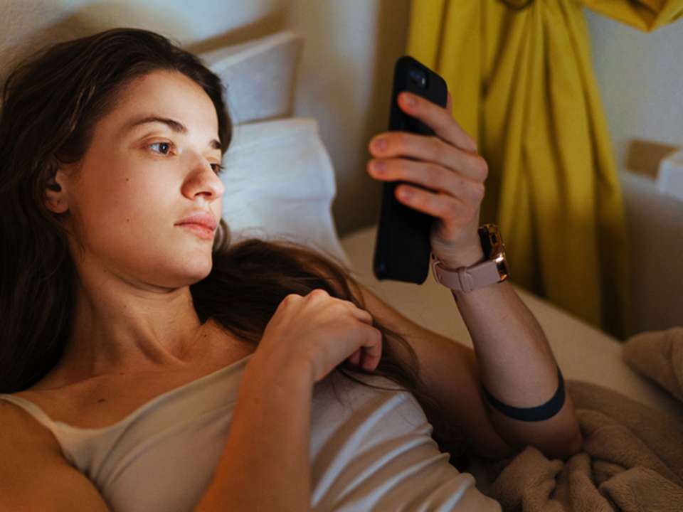 A woman lying in bed looking at her phone.