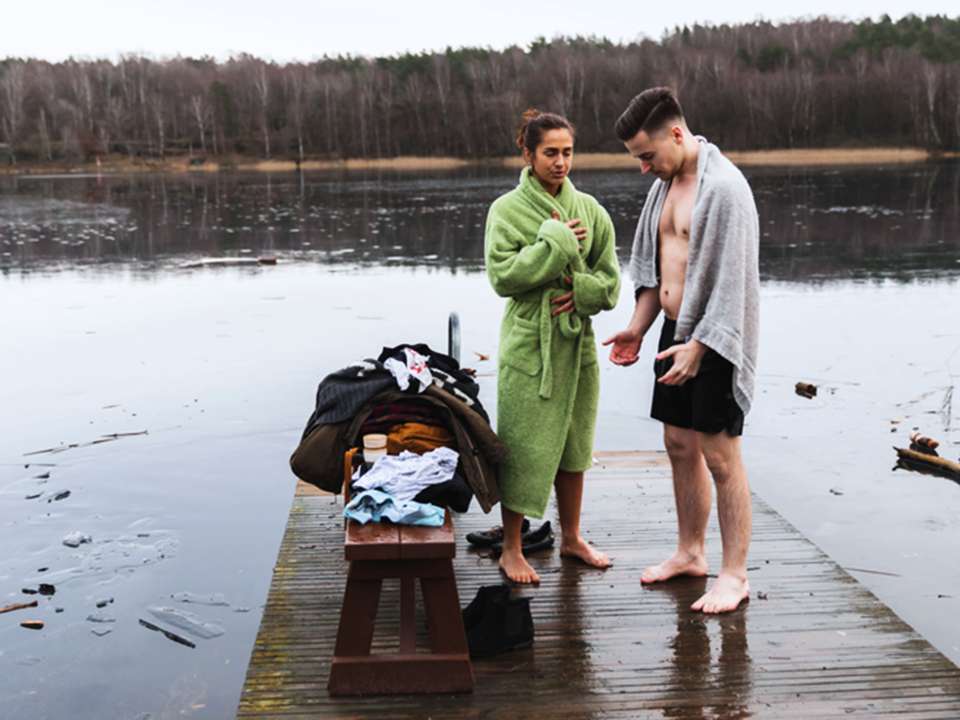 Two people stand on a dock after a cold plunge in a lake.