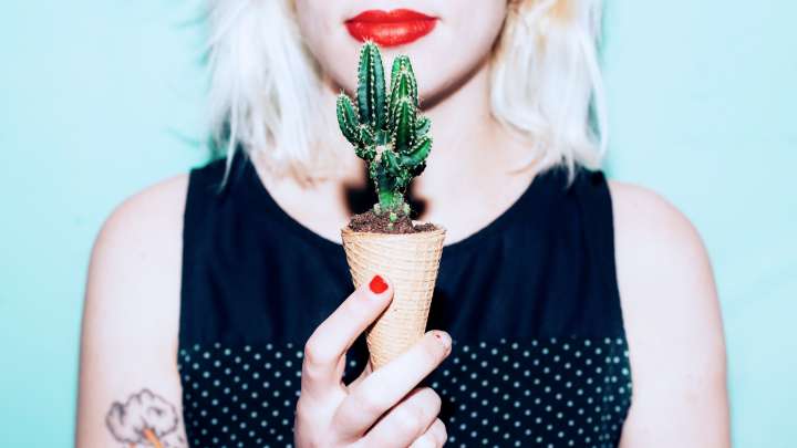 A woman holds a cactus in an ice cream cone.