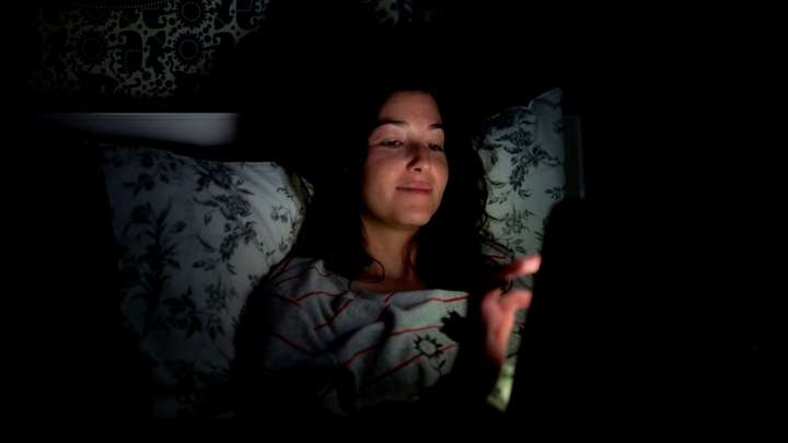 A woman uses a tablet in bed in the dark.