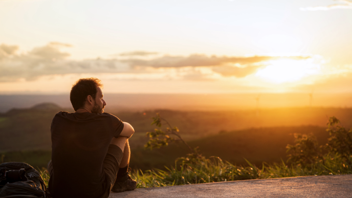 A photo of a man sitting down and looking at the sunset