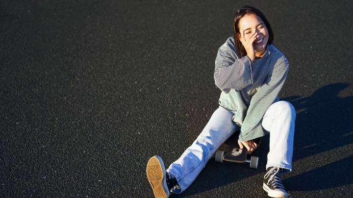 A woman laughs after falling off a skateboard.