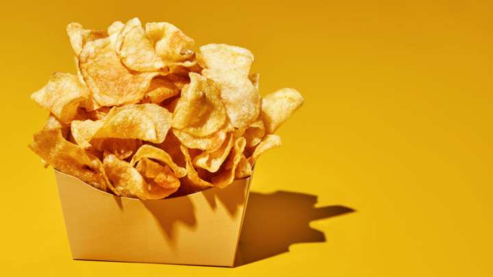 An overflowing box of potato chips on a yellow background.