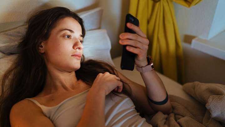 A woman lying in bed looking at her phone.