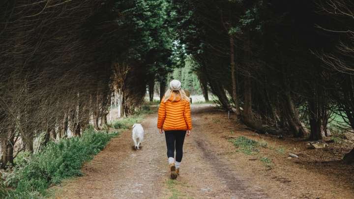 Woman in orange jacket walking her dog down a path