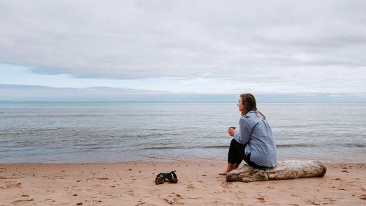 A woman sits on the beach alone.