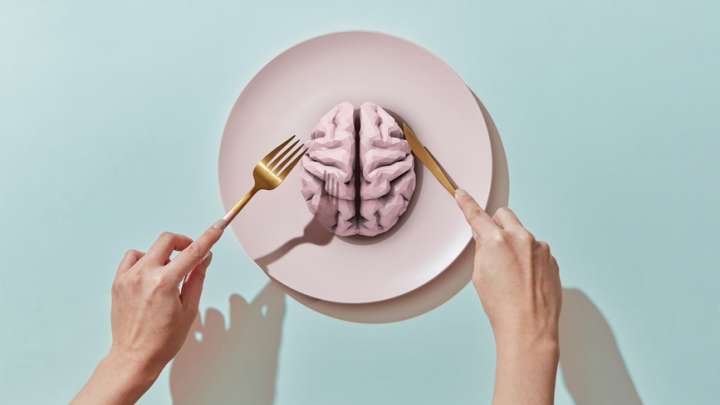 Hands holding a knife and fork over a plate with a brain