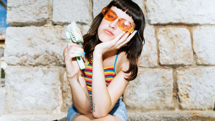 A woman holds a small fan up to her face.