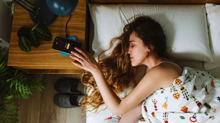 A woman lying in bed reaches for her phone alarm.