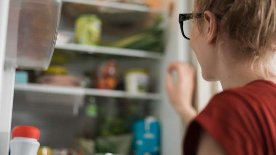 woman standing in front of her opened refrigerator looking in at a selection of vegetables
