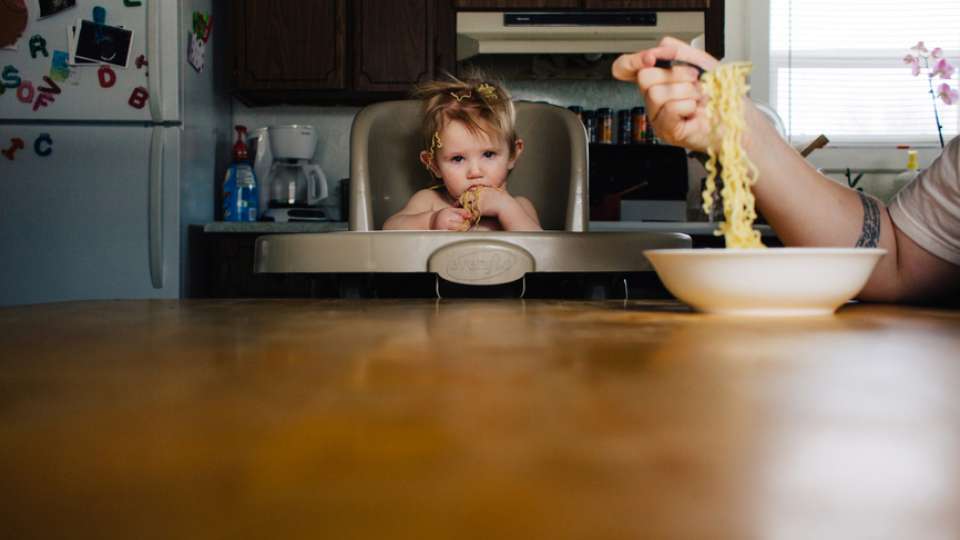 Toddler in high chair at table with spaghetti on head