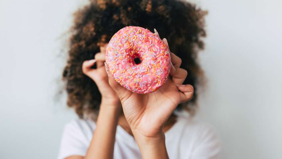 a woman holding a strawberry donut in front of her face