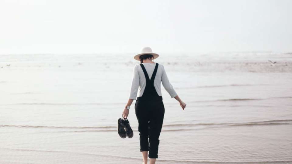 Woman in hat walks in shallow ocean water
