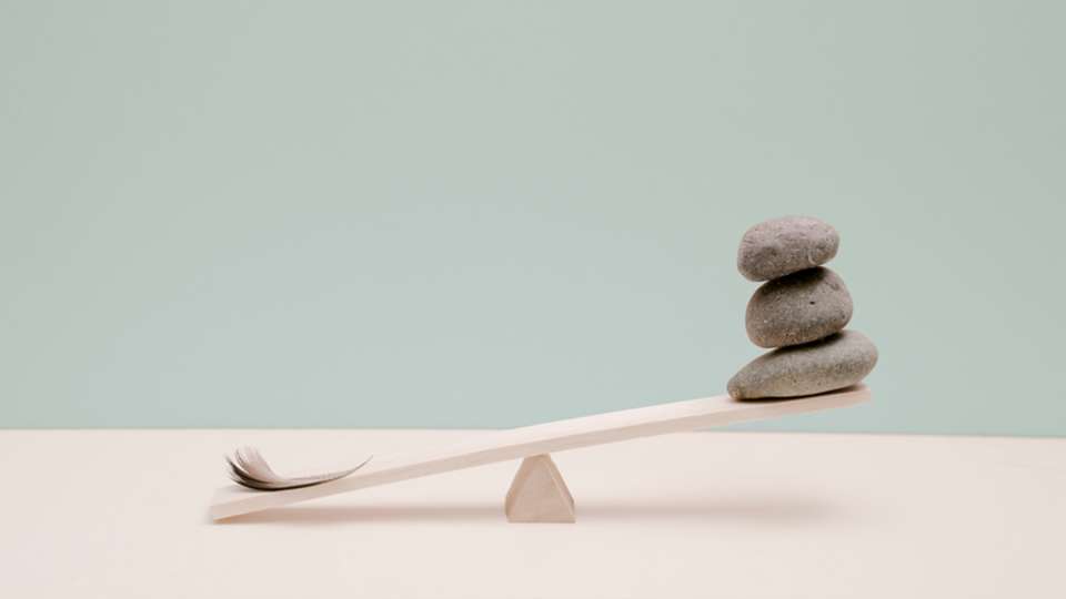 an unbalanced scale with a feather and rocks on it