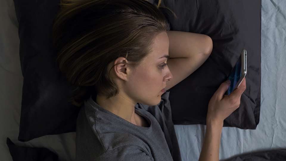 a young woman lying in bed looking at her phone
