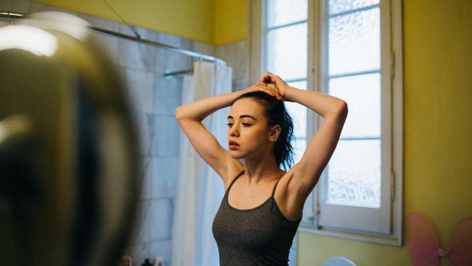 Woman looking in mirror with hands over head