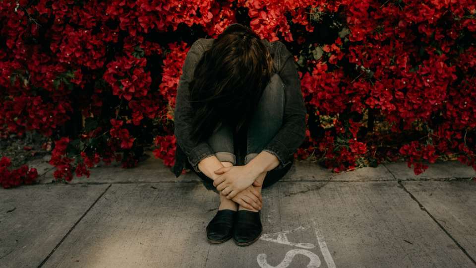 Woman with head down sitting amidst red flowers