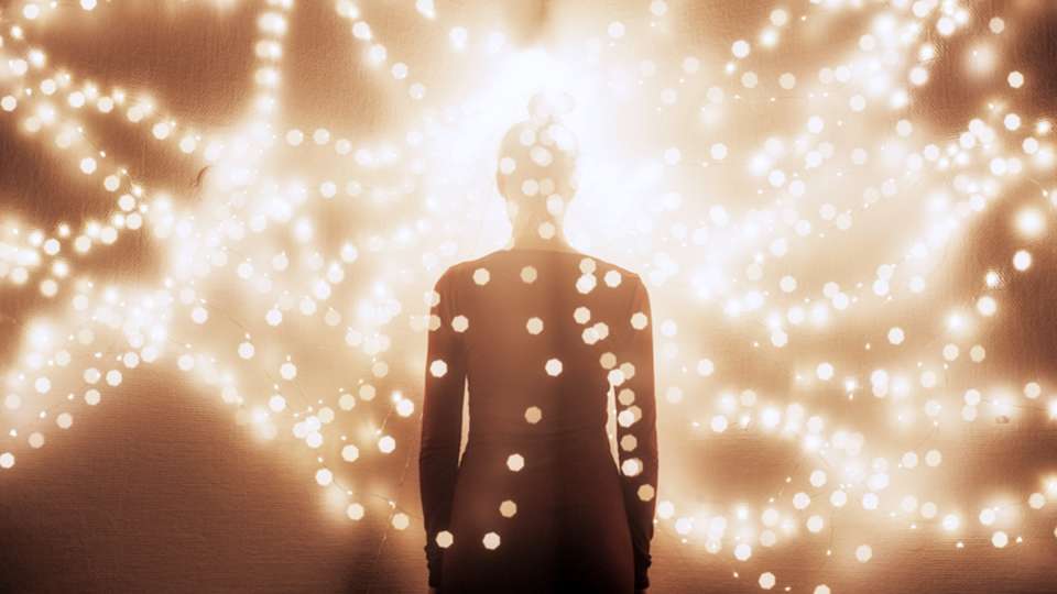 A woman's silhouette stands surrounded by glowing string lights.