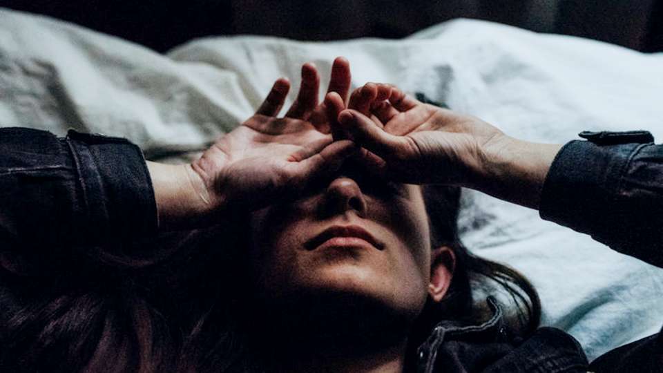 A woman with a headache lies down on a bed.