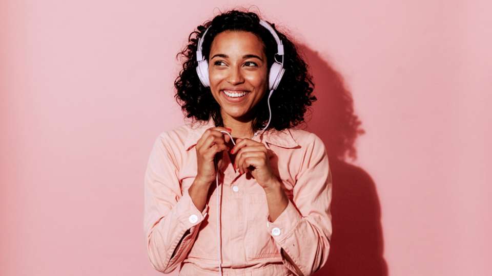 Woman listening to headphones with pink backdrop