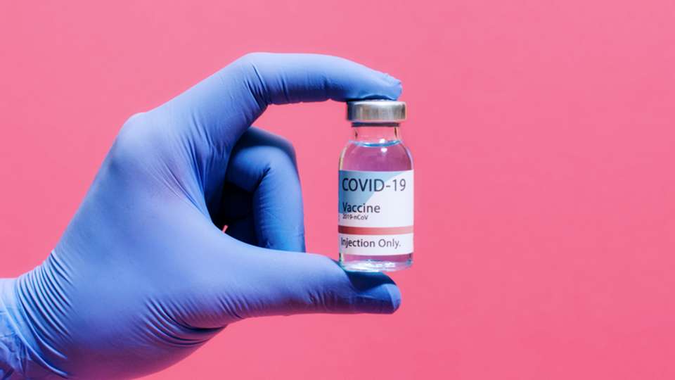 gloved hand holding COVID vaccine vial