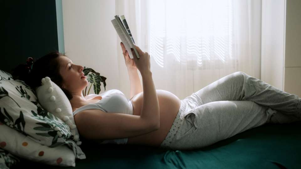 pregnant woman reading a book in bed