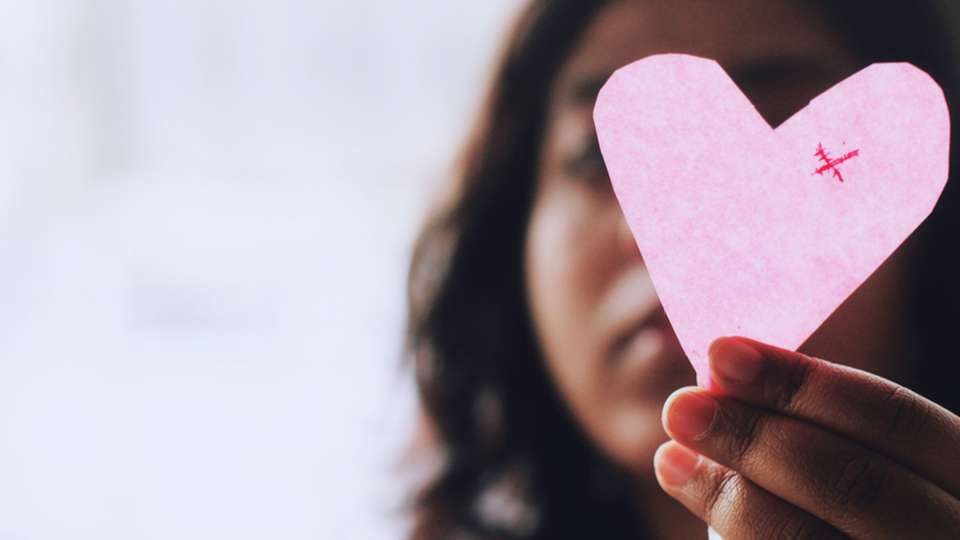 A woman holds up a paper cutout of a heart.