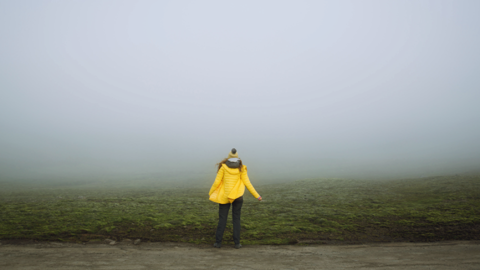 A woman standing in thick fog facing away from the camera