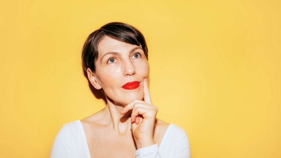 A woman looks thoughtful against a bright yellow background.
