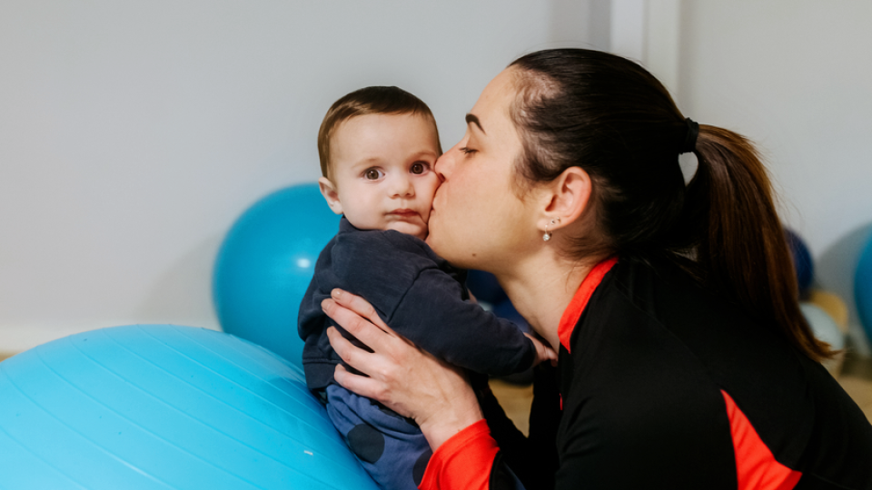 A woman kissing her baby who sits on an exercise ball