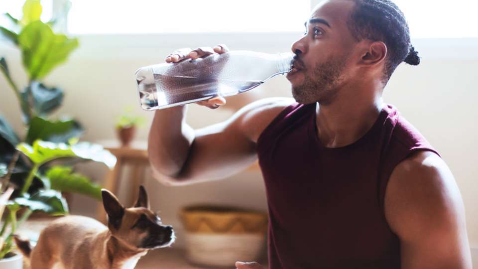 A man drinks water after working out while his dog looks on.