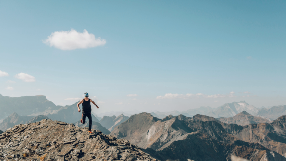 A photo of a man running along a mountain ledge