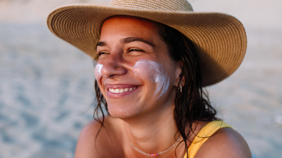 A woman sitting on the beach with sunscreen on her face