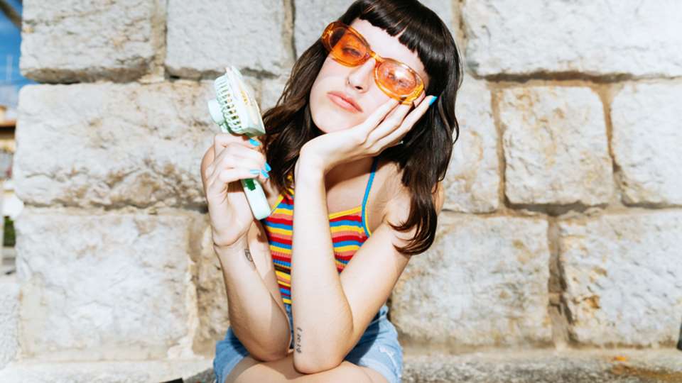 A woman holds a small fan up to her face.