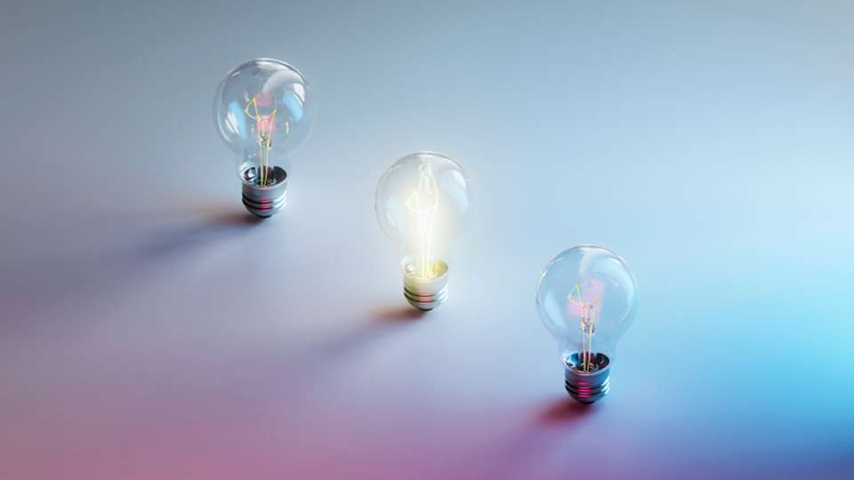 Three lightbulbs, one lit, on a hazy blue and pink background.