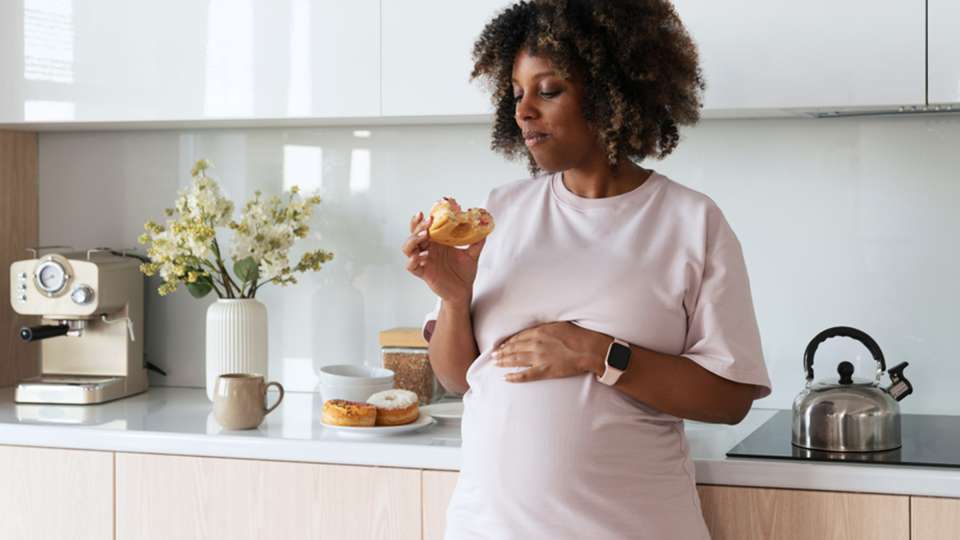 A pregnant woman eats a donut.