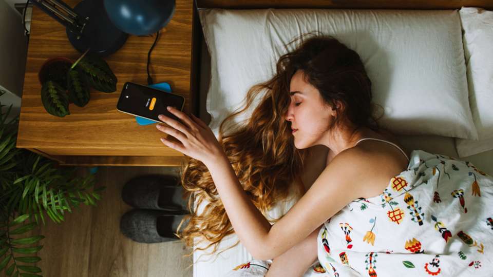 A woman lying in bed reaches for her phone alarm.