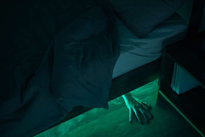 In the dark, a creepy hand reaches out from under a bed.