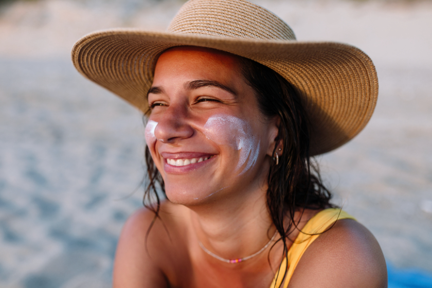 A woman sitting on the beach with sunscreen on her face