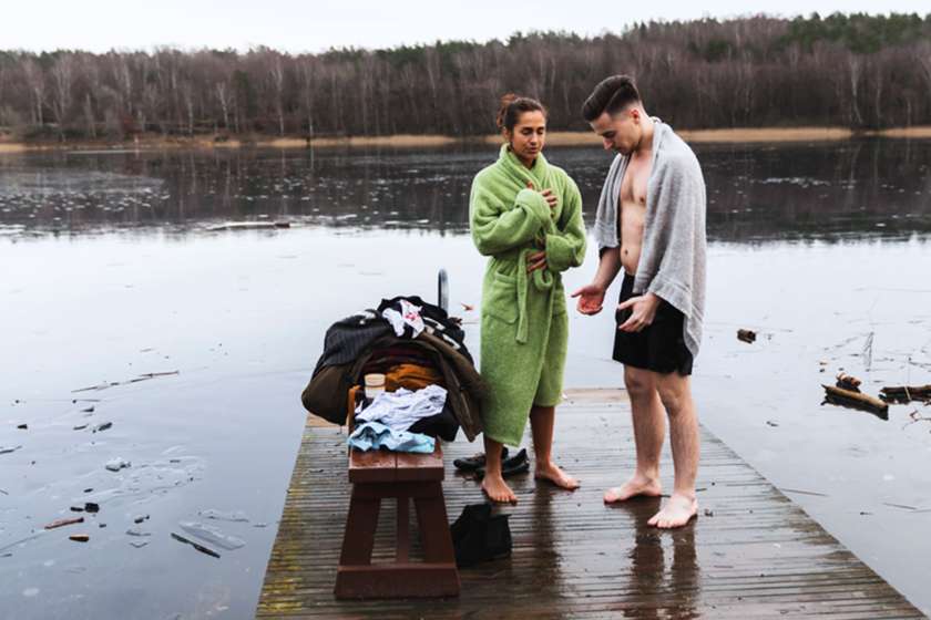 Two people stand on a dock after a cold plunge in a lake.