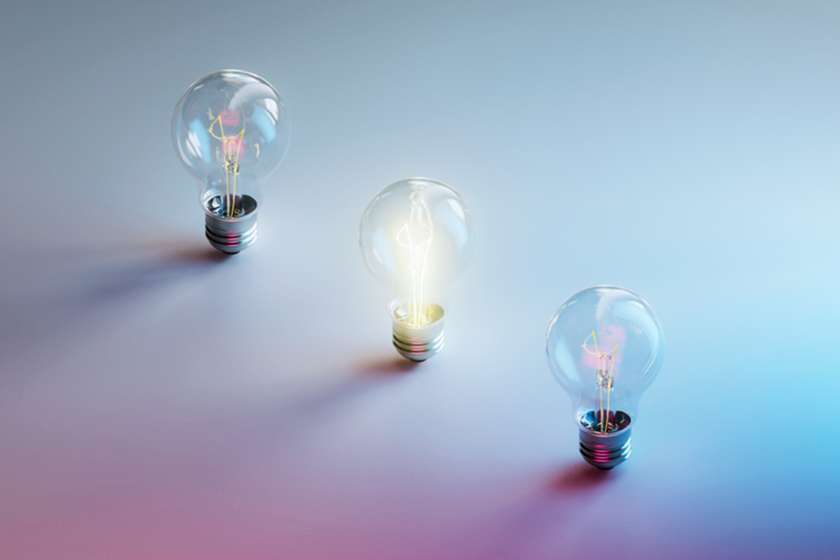 Three lightbulbs, one lit, on a hazy blue and pink background.