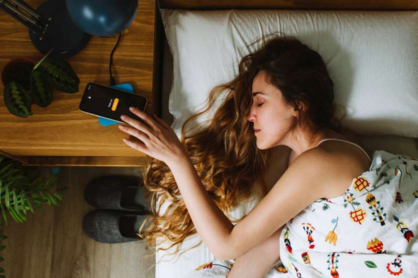 A woman lying in bed reaches for her phone alarm.