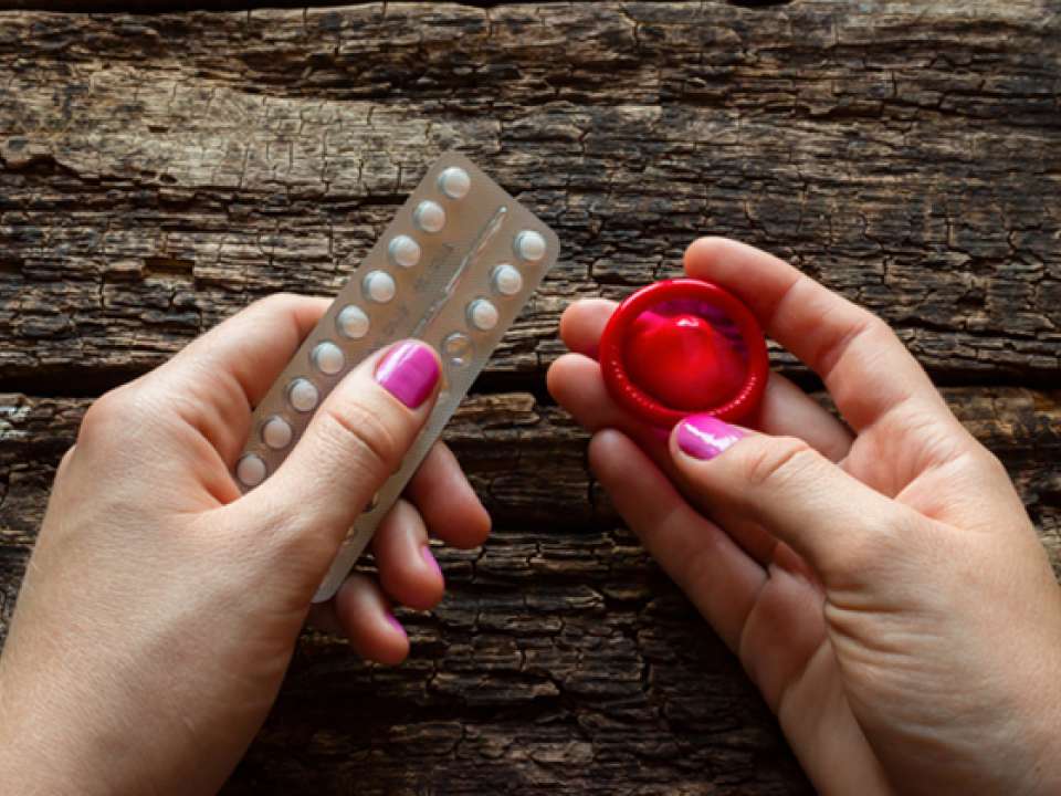 Female hands holding a package of birth control pills and a condom