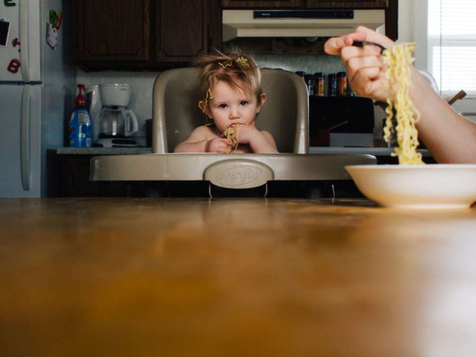 Toddler in high chair at table with spaghetti on head