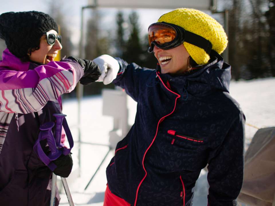 A skier and a snowboarder are smiling and fist bumping as they wait in line to get on the chairlift.